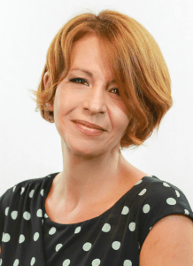 A woman with red hair and polka dots is smiling.