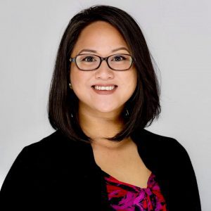 A woman with glasses and black jacket smiling.