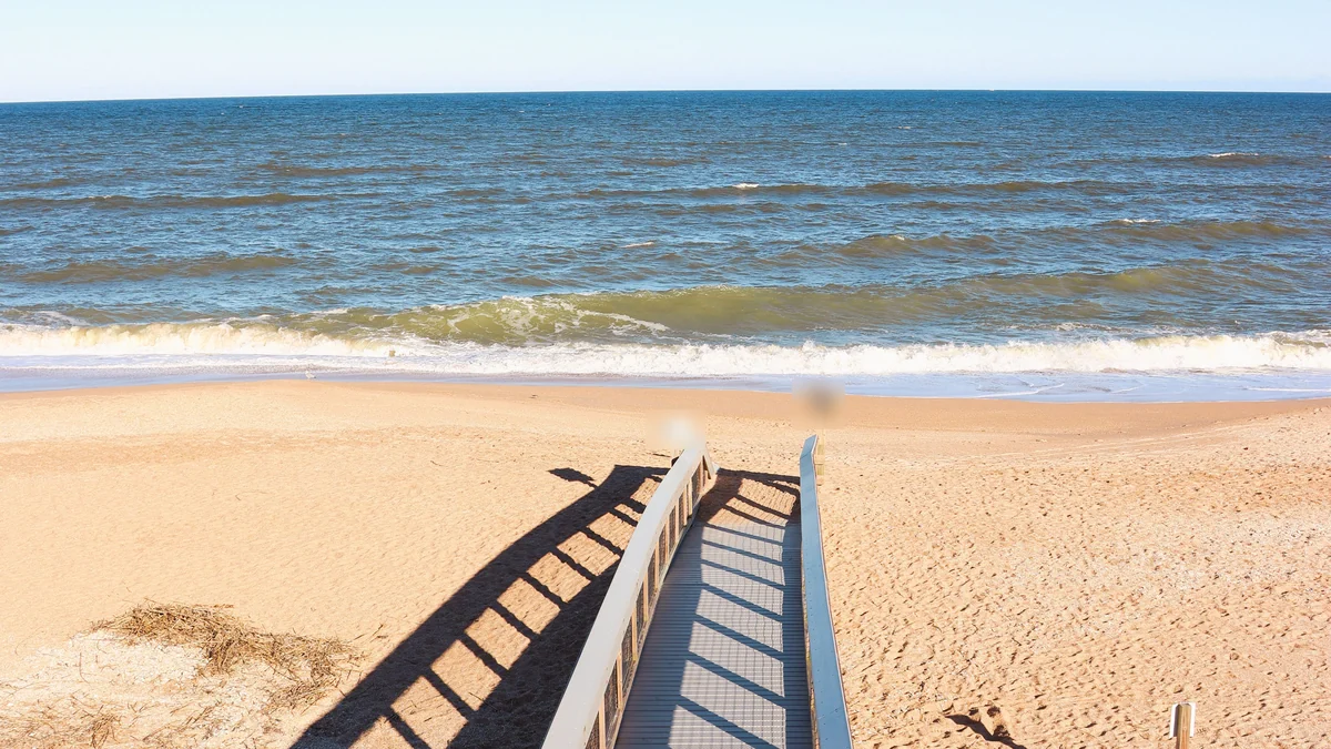 A wooden dune walkover that runs down to a sandy beach and the ocean under a blue sky