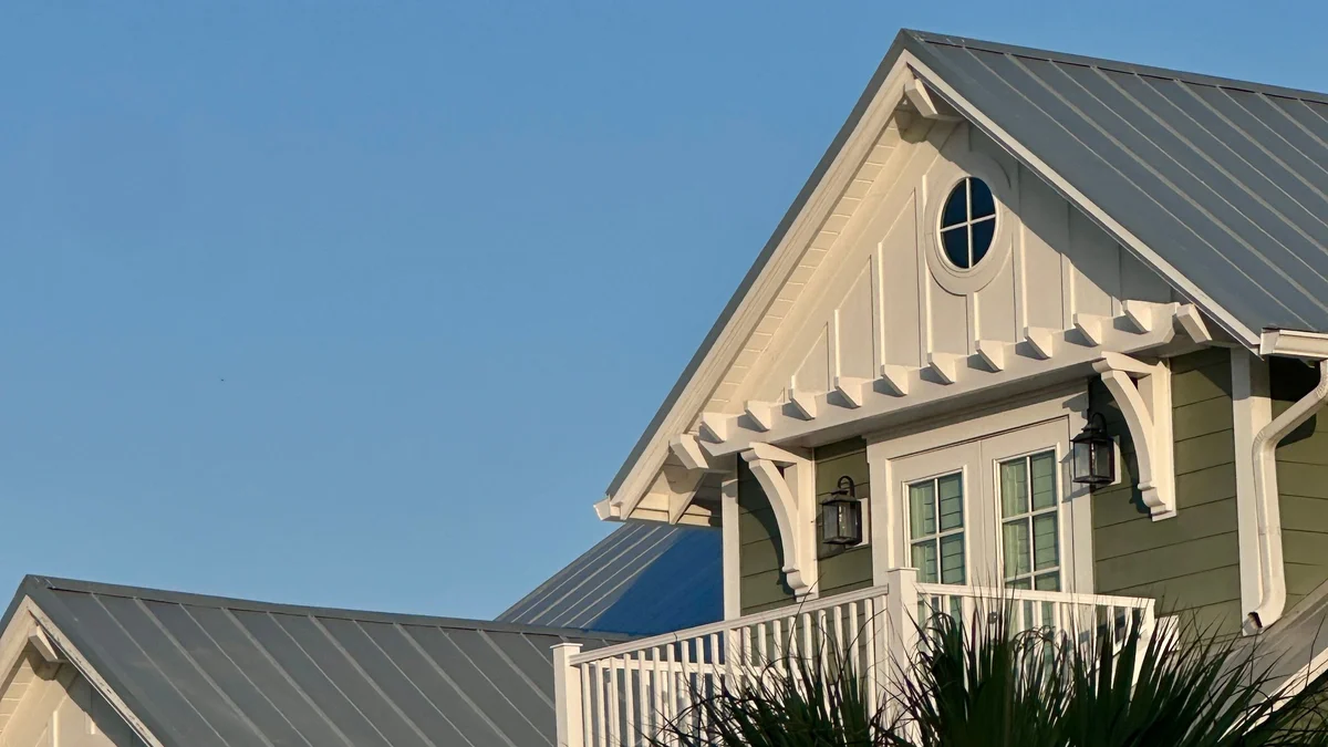 Gray metal roofs on a light green house with white trim, palm fronds and a clear blue sky