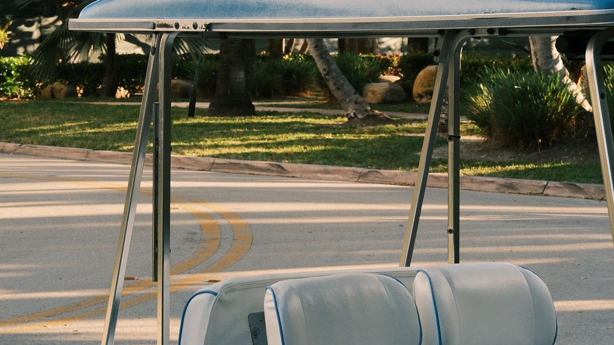 A light blue golf cart parked by a curb on a sunny street lined with grass, shrubs and palm trees